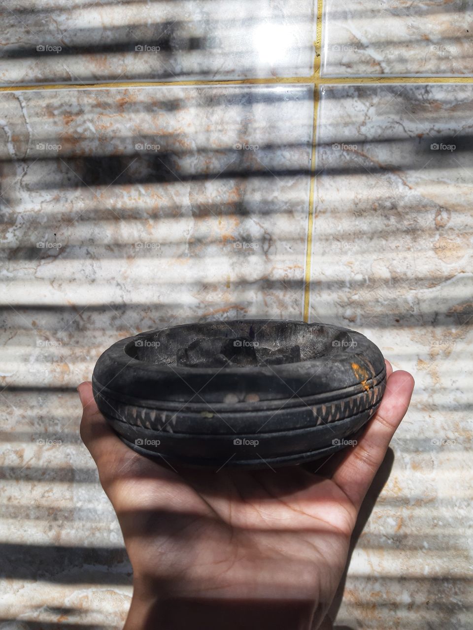 A black wooden ashtray is being hold by a hand