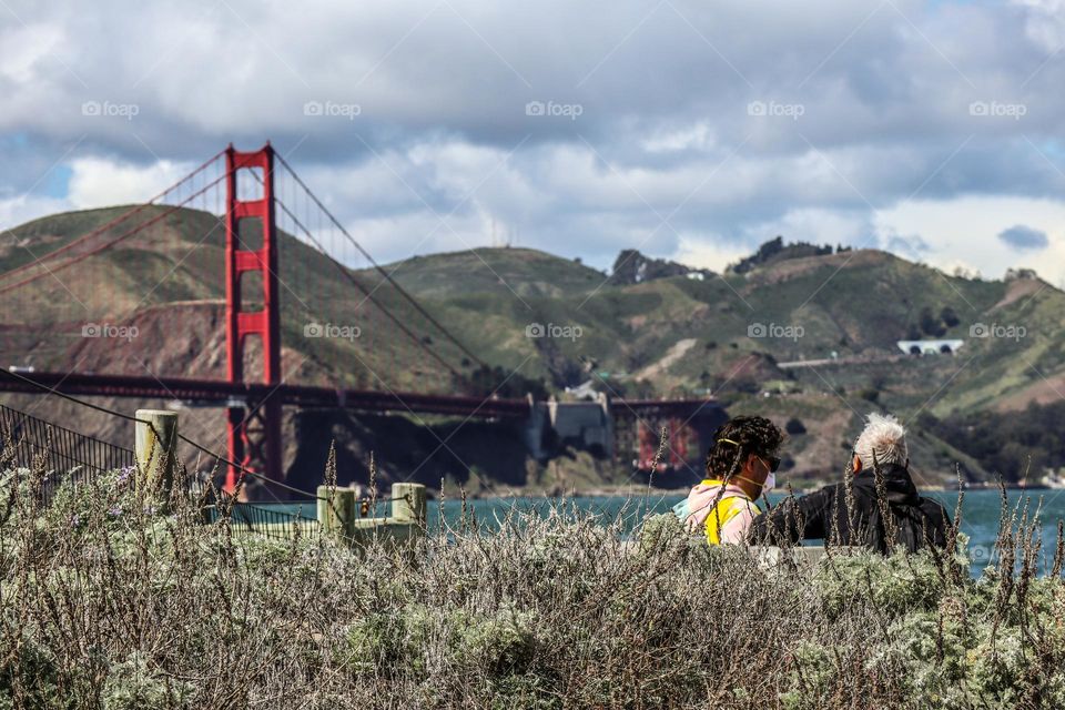 Couple relaxing on a warm day in San Francisco California viewing the Golden Gate Bridge on the bay from crissy field 