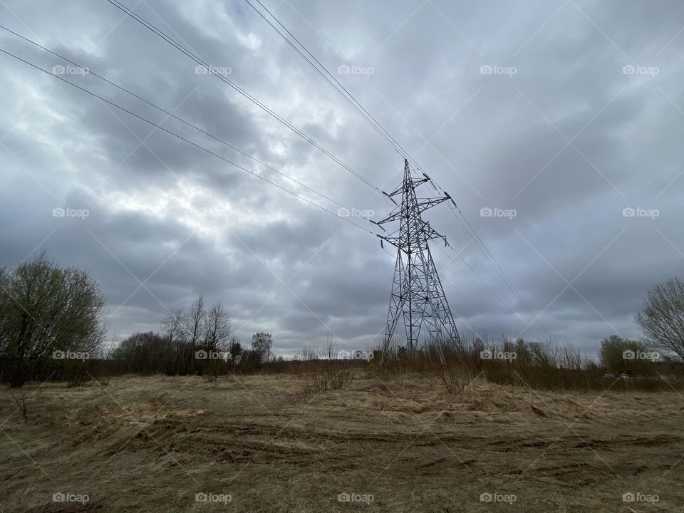 An electricity post in the middle of a field. Stormy clouds in the background. A moody picture. Industrial and abandoned.