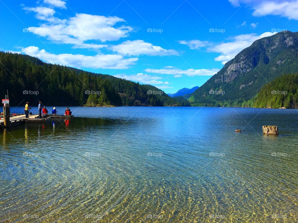 Mountains and rippling lake in beautiful British Columbia Canada, brilliant blue cloud dotted sky, fishing dock; calm, serene crystal clear water, room for text, concept travel vacation, rest and relaxation, nature and outdoor activities 