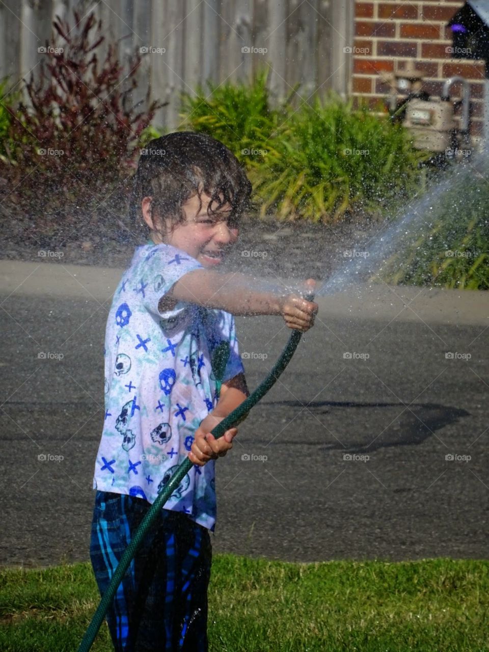 boy playing with the garden hose spraying water up into the sky
