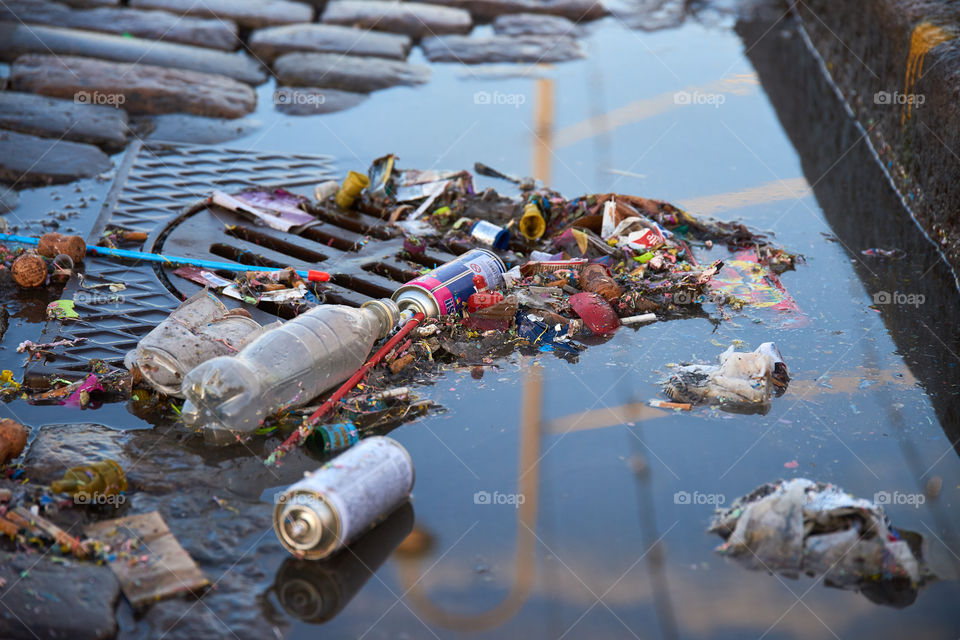 Helsinki, Finland - May 1, 2017: Plastic and other trash over sewer and partly floating in a puddle on cobble street after first of May celebrations.