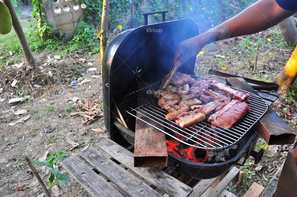 Pork ribs, premium portions of bacon and blade loin roasts cooking on a grill. Outdoor cooking. Cookout dinner.