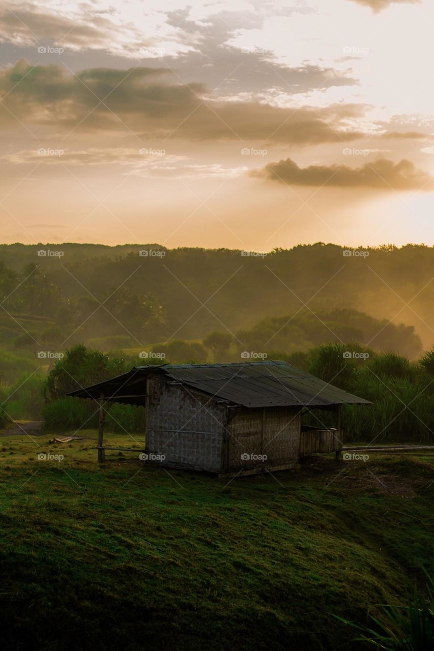 a small house in the middle of a hill with a sunrise that makes the atmosphere warm and fresh