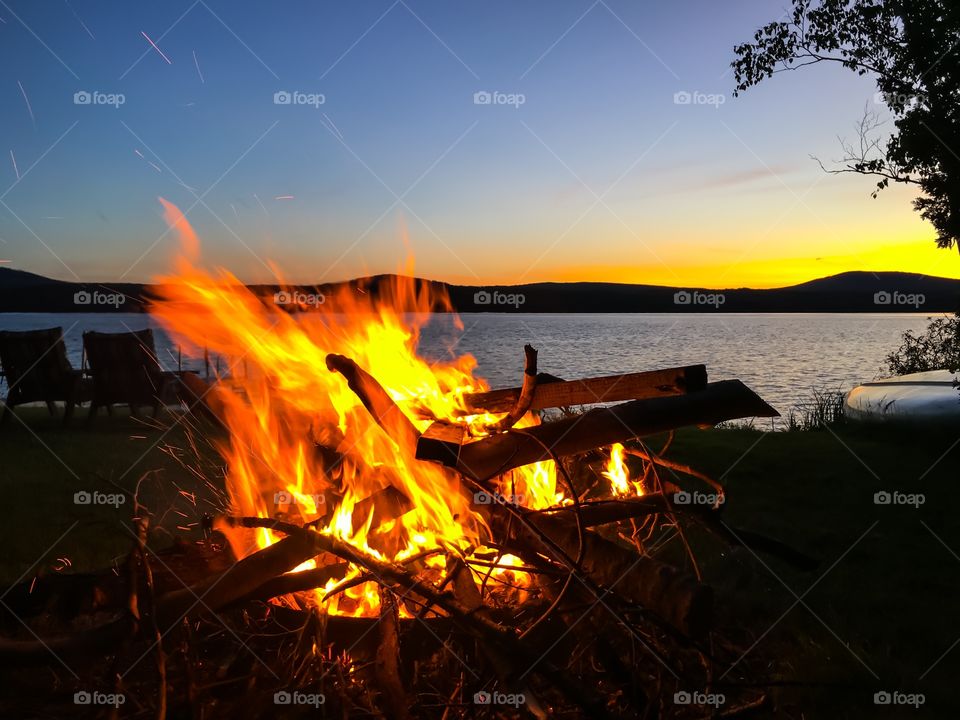 Burning camp fire by lake in Adirondack mountains, New York State, at sunset