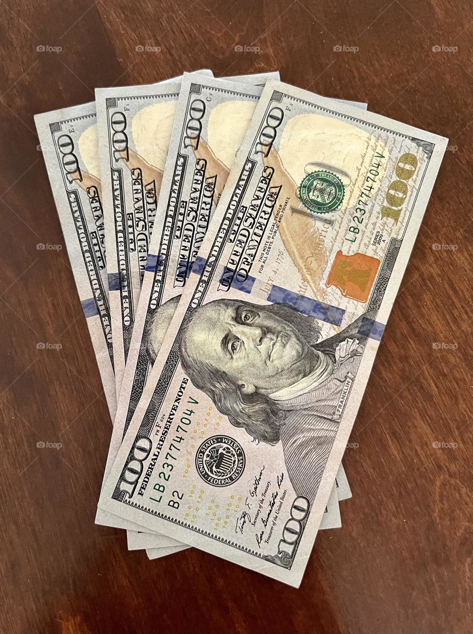 Four one hundred dollar bills fanned out on a wood table top.  Money to spend, work for, green money to earn with hard work.  Franklin is pictured.