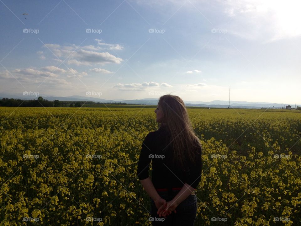 A girl in the field with yellow flowers from the back