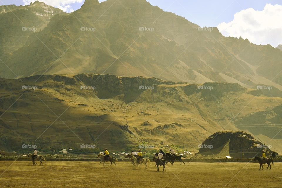 kashmiri local people playing horse polo in summer against dramatic golden brown mountain landscape