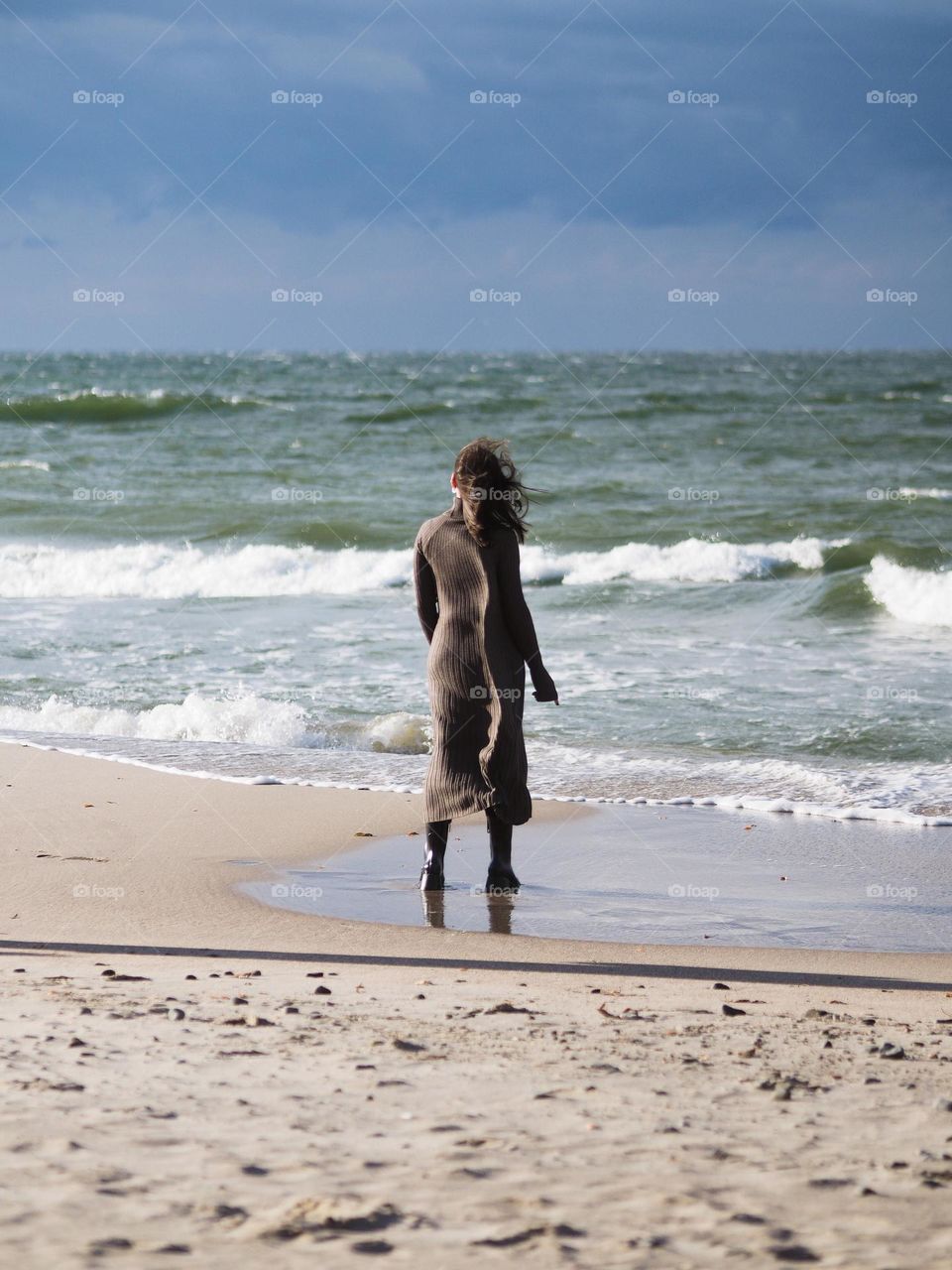 Young woman with dark long hair wearing brown dress on seaside in sunny autumn day.