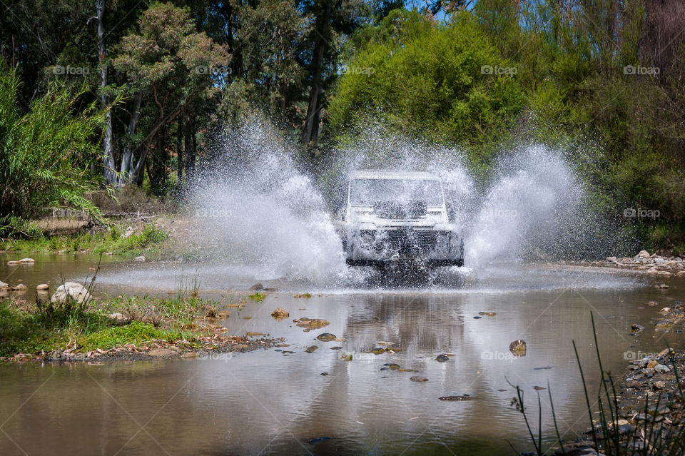4x4 vehicle crossing stream on speed splashing water from under wheels.