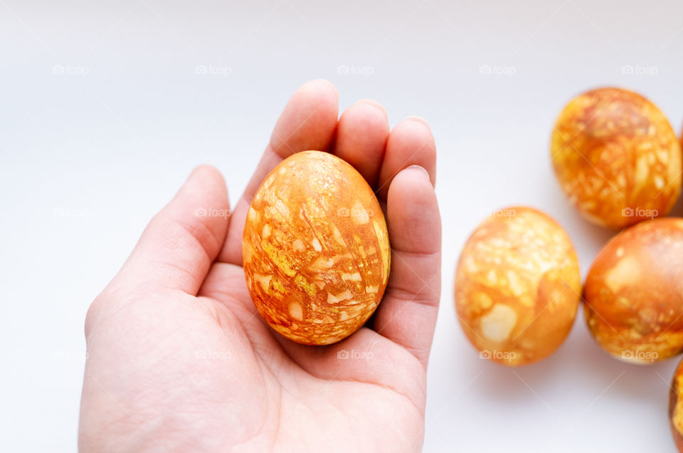 Top view of human hand holding an orange Easter egg on a white background.