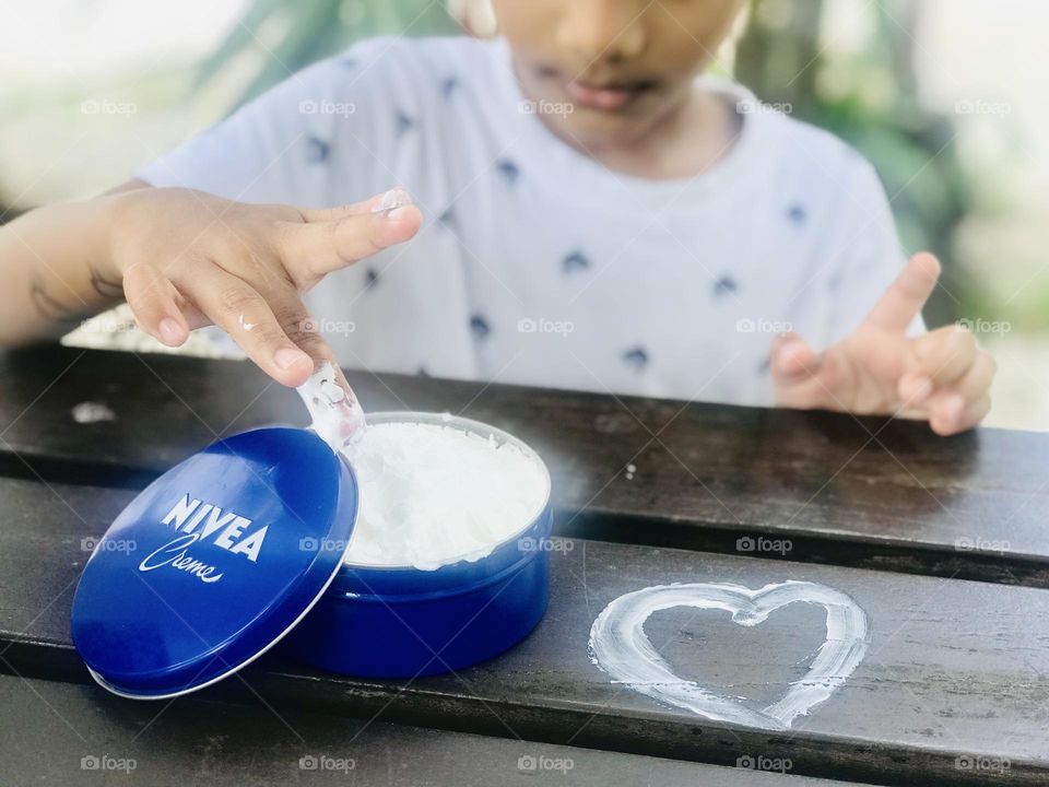 Nivea cream box opened and a love symbol drawn with cream by a boy.a finger dip into the cream.