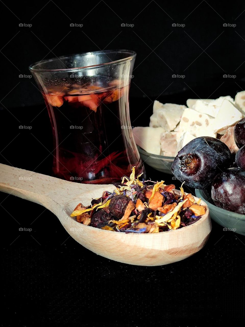 Composition. Tea drinking in Baku style. A wooden spoon with a mixture of black tea and various herbs, a glass of "armuda" with tea, a saucer of dates and a saucer of walnut baklava