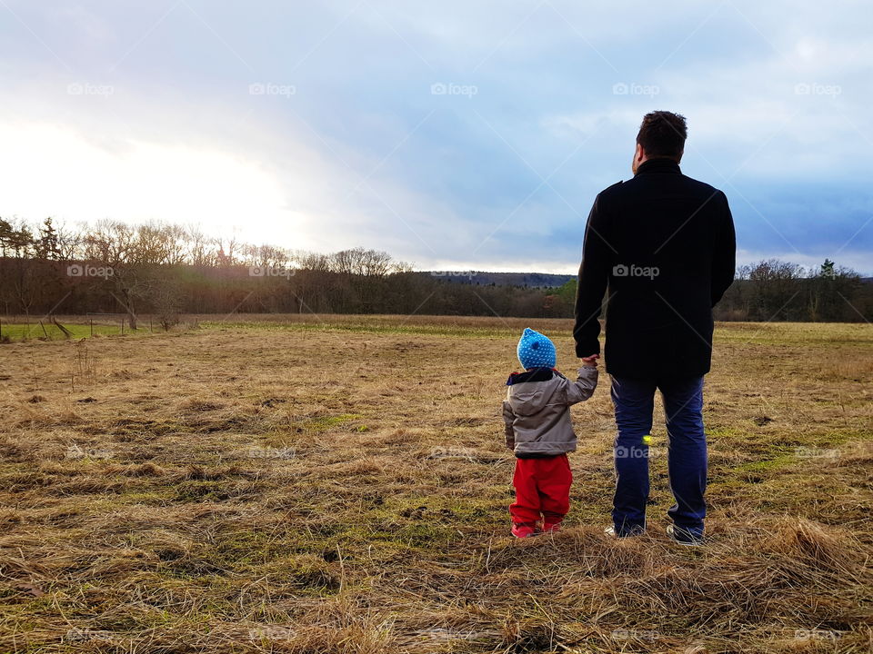 Dad and daughter. Hand in hand. On a field in autumn, watching the sunset.