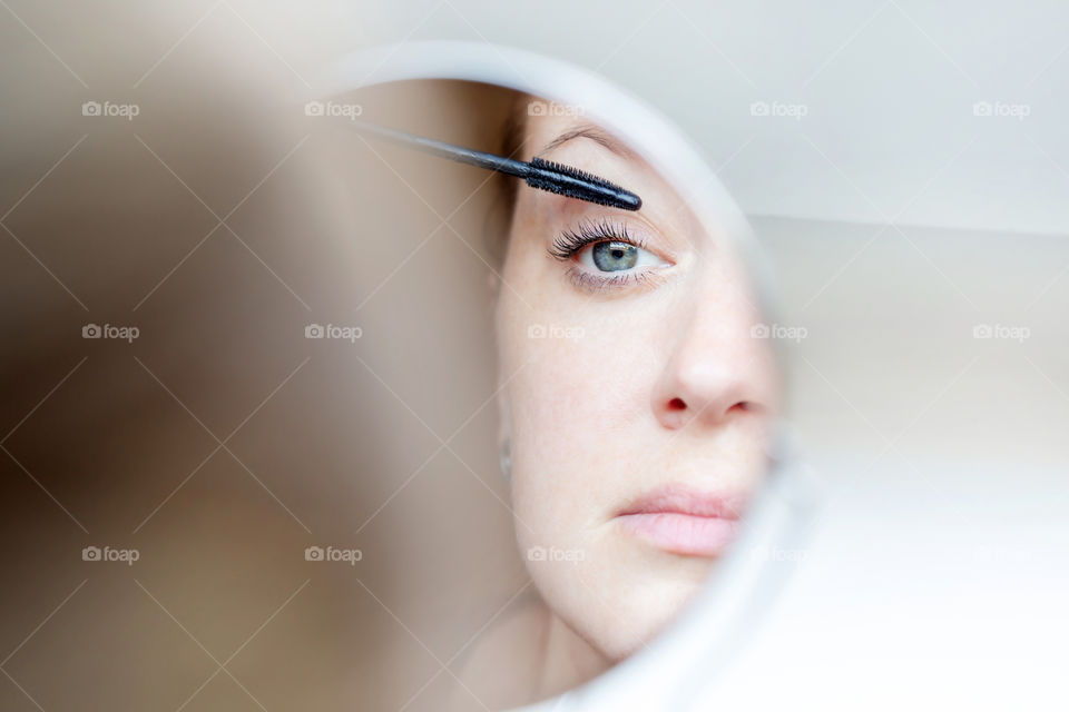 Young woman applying mascara to her eyes looking in the mirror