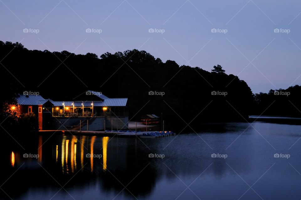 A beautifully lit boathouse casts vivid reflections on the water’s surface during the early morning twilight. Lake Johnson Park is a outdoor jewel in Raleigh North Carolina.