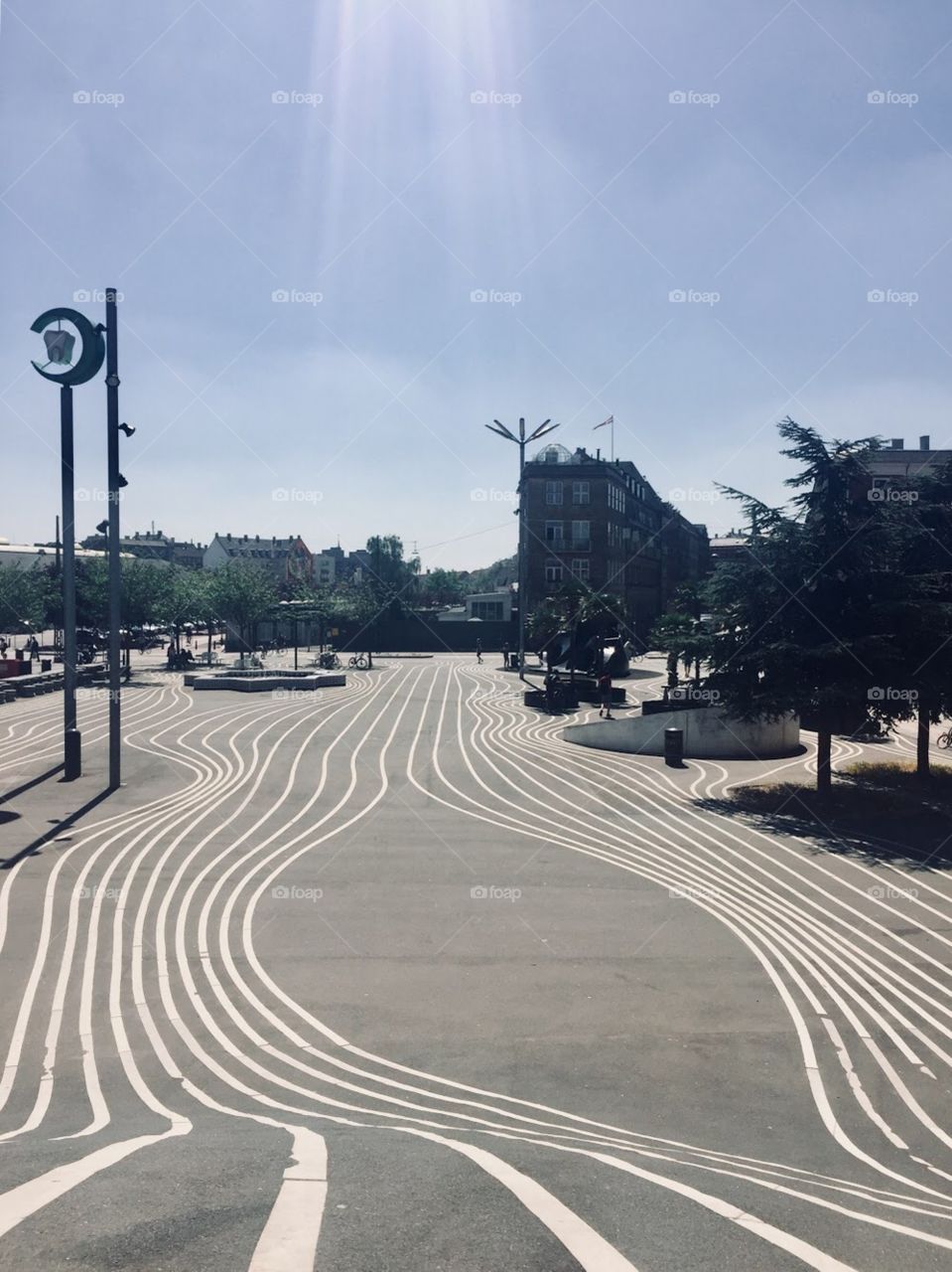 Urban park with black asphalt has crisp, symmetric, white lines leading up a hill. Art installations are on either side of the road. 