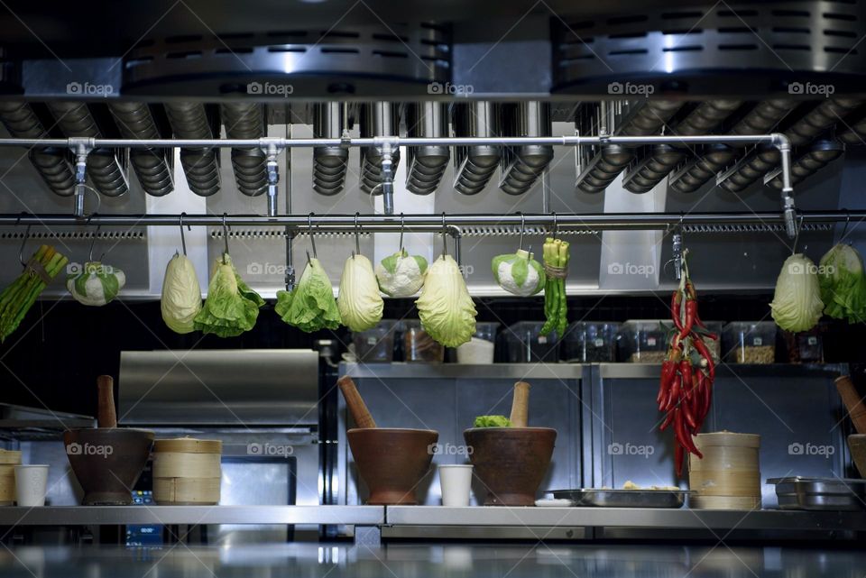 Modern kitchen with metal equipment.  A variety of vegetables are hung on metal rods.