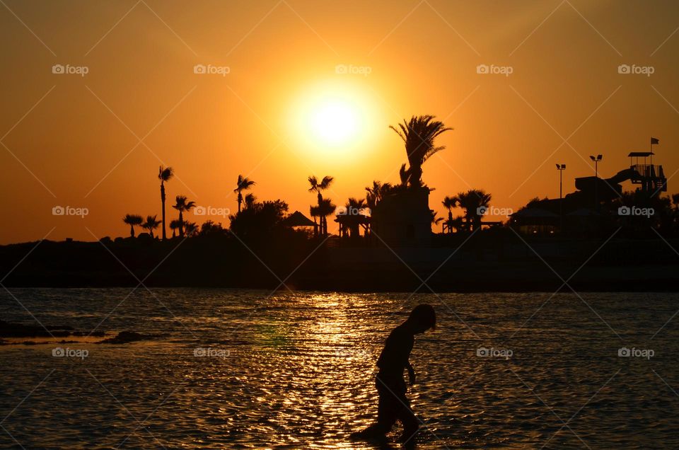 a boy in the sea against the background of a beautiful sunset