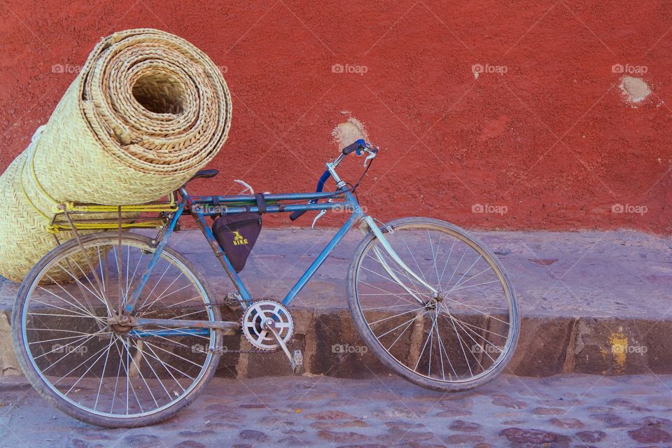 A bicycle is parked on a cobble stone street leaning on the straw mat cargo,