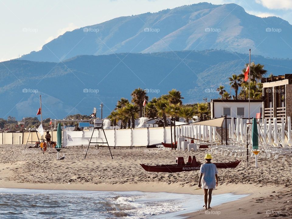 a woman walks by the sea in summer at sunset