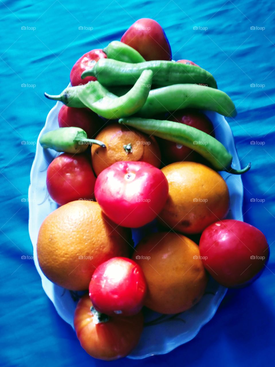 A dish of tomatoes, green peppers and oranges a variety of vegetables and fruits