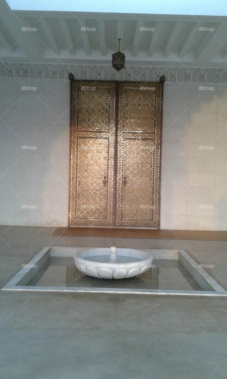 a fountain in front of a large golden
 door of a mosqe