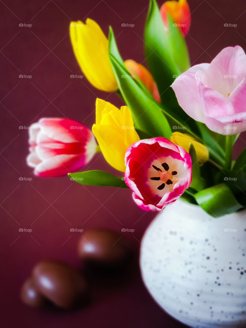 Spring bouquet. Multi-colored tulips in a white clay jug with chocolate eggs on a brown background. Easter holidays. Horizontal orientation