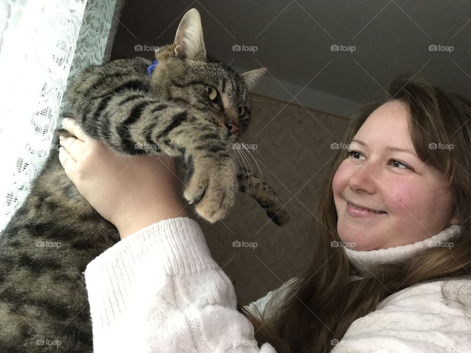 A girl is holdin a cat and smiling.