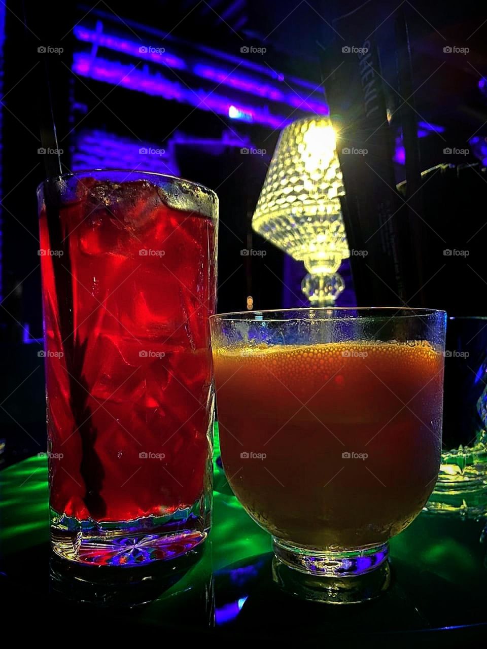 Summer treats. Restaurant. A table with two glasses of refreshing cocktails. Orange cocktail "Pop Corn" from coffee liqueur, orange and corn. Red glass "Chinese High Ball" of hibiscus, lemongrass, baijiu (Chinese vodka) and pieces of ice