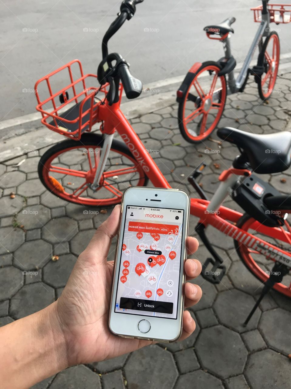 user is using application on iPhone for “mobike” rental bicycle which parks on footpath beside road, Chiang Mai, Thailand