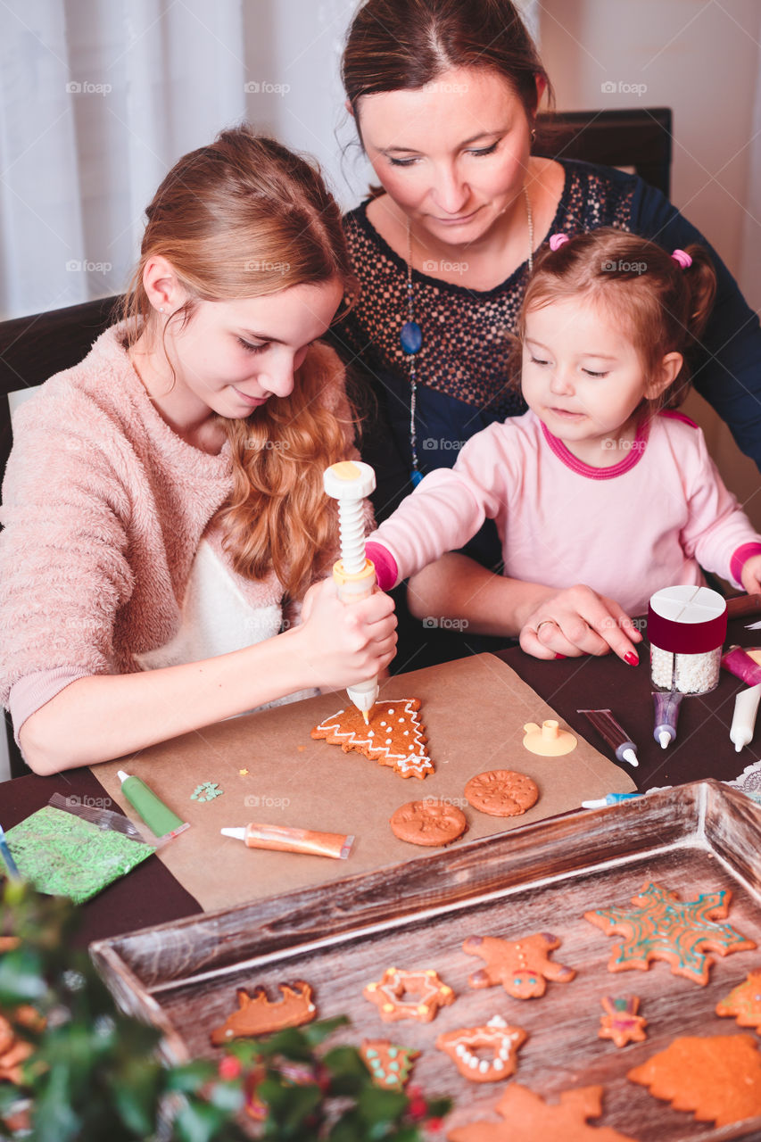 Family decorating baked Christmas gingerbread cookies with frosting