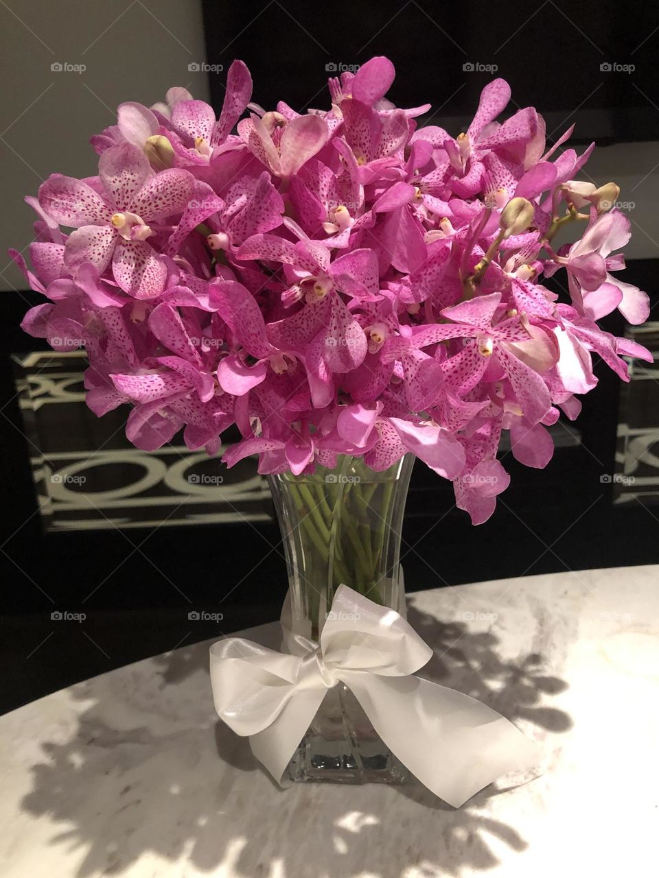 Pink orchids in a crystal Basel wrapped with a white ribbon on a marble table 