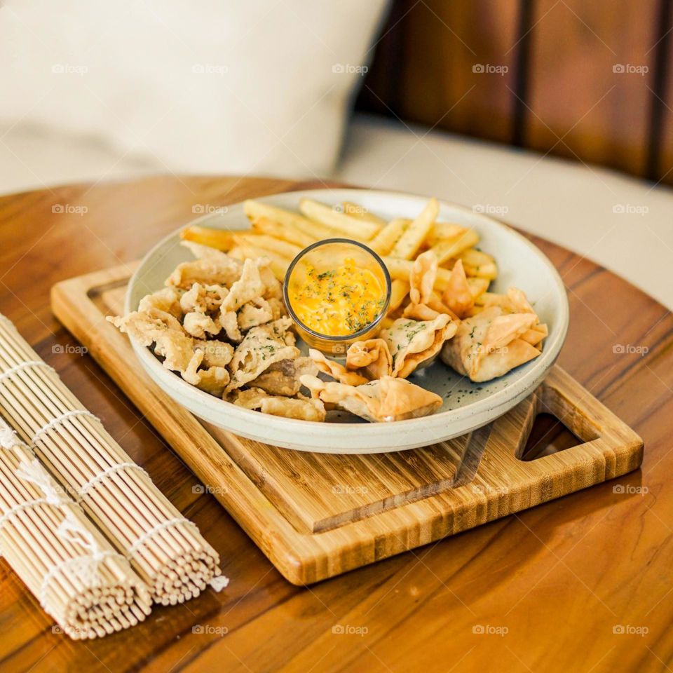 Fried potatoes and dumplings on a plate with a combination of cheese sauce. Eat. Food. Snack. Café. Photography. Table. Wood. Motive. Wood motif. Potato. Dumplings. Fried food. Crispy. Cutting board.