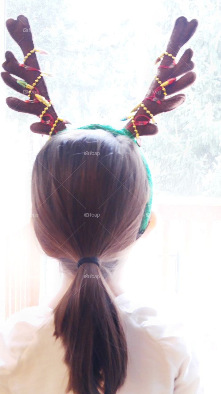 little girl wearing reindeer antlers looking out a window