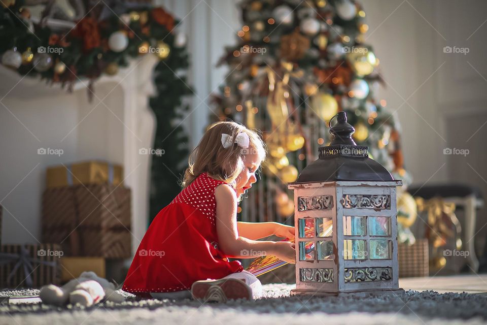 Little girl in the evening plays with a lantern at home by the fireplace