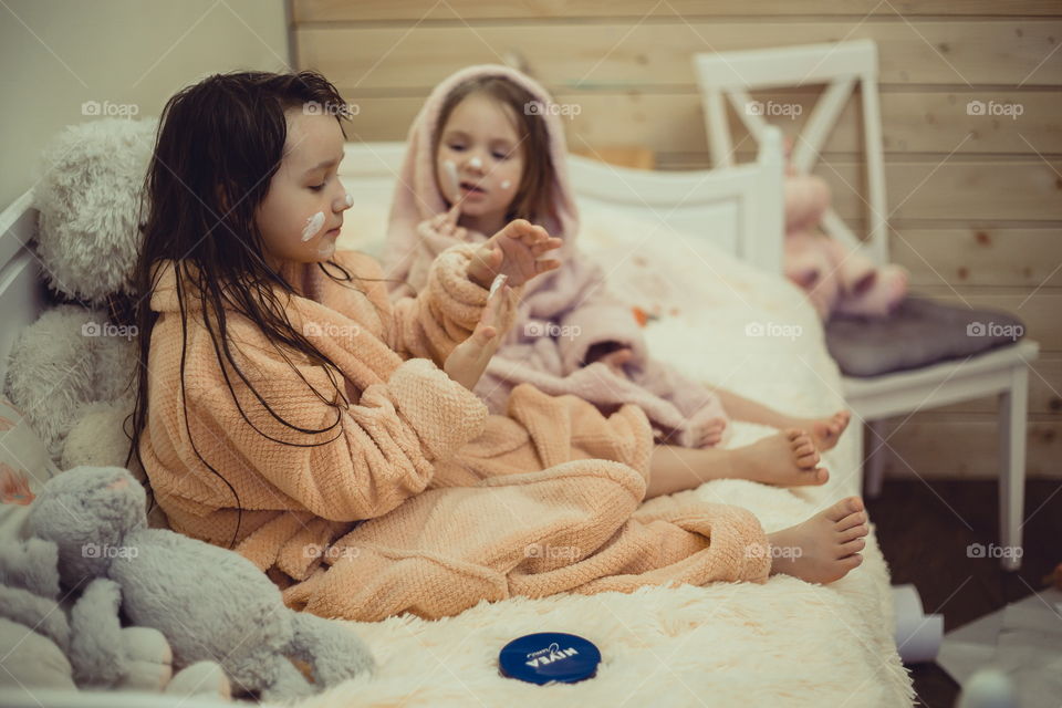 Little sisters in bathrobe with cream