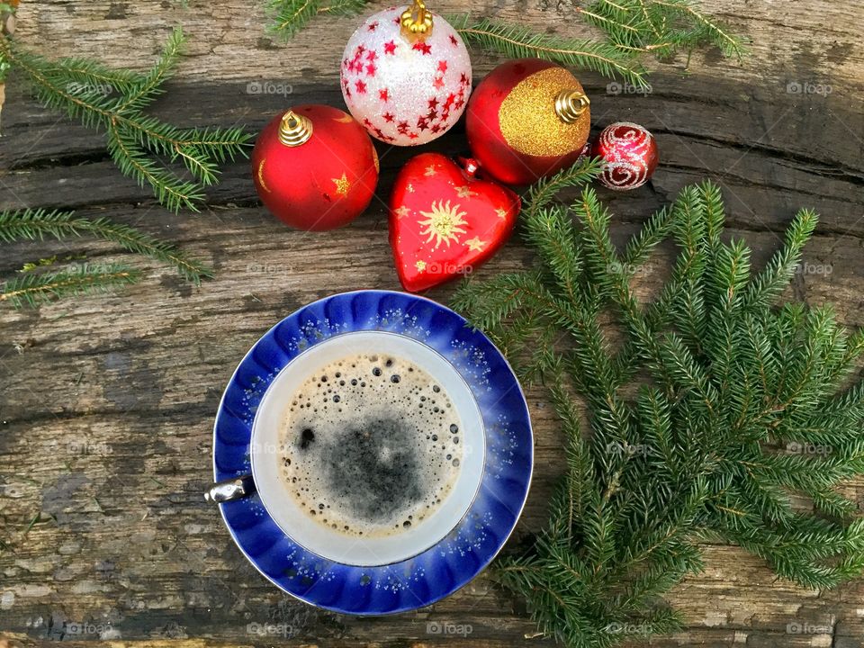 Cup of coffee on wooden table  surrounded by pine cone tree branches and red glittering globes