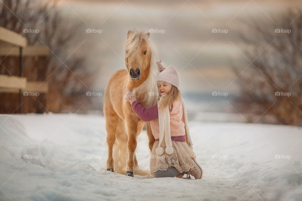 Little girl with palomino pony at winter sunny day