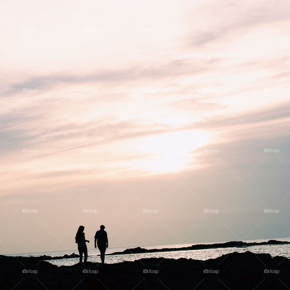 Silhouette of couple on beach against dramatic sky