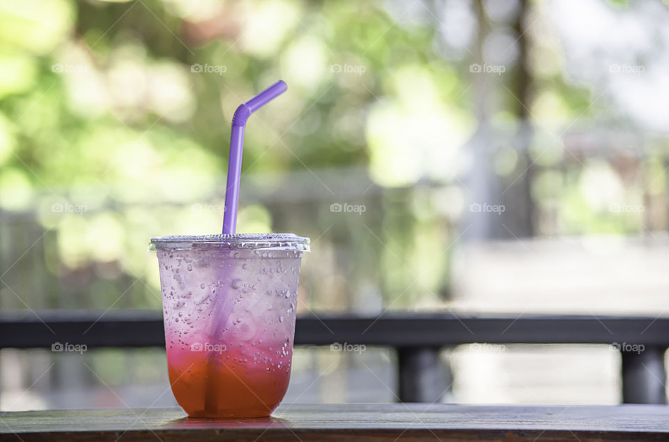 Red juice with ice in a plastic glass on table.