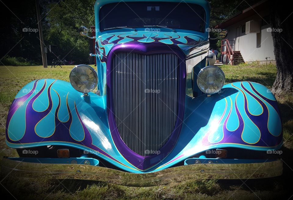 a classic hot rod displayed at a car show with beautiful purple flames and purple around the grill. Notice the reflection on it low bumper