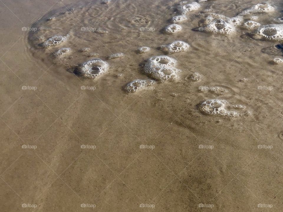 Closeup of ebbing wave bubbles and swirls on sand 