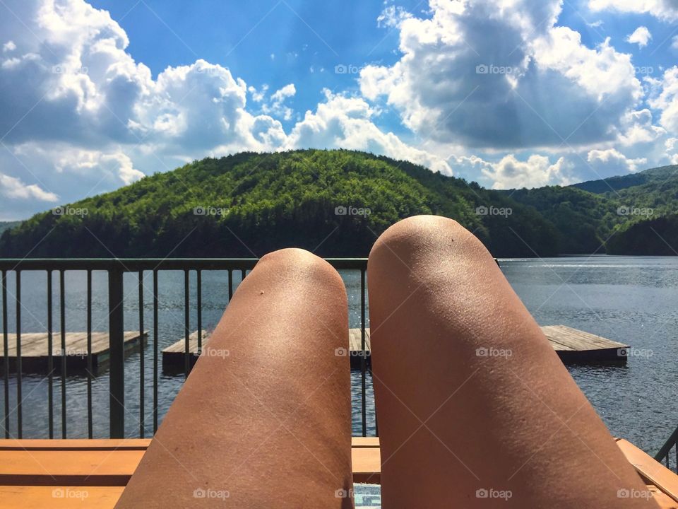 Let's get tanned - woman's legs and lake surrounded by forest 