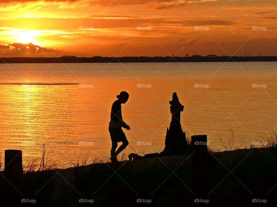 A silhouette of a man with a hat on strolls along the beach in the late evening sunset. The waters surface was shimmering and glazed over by the last light of the night