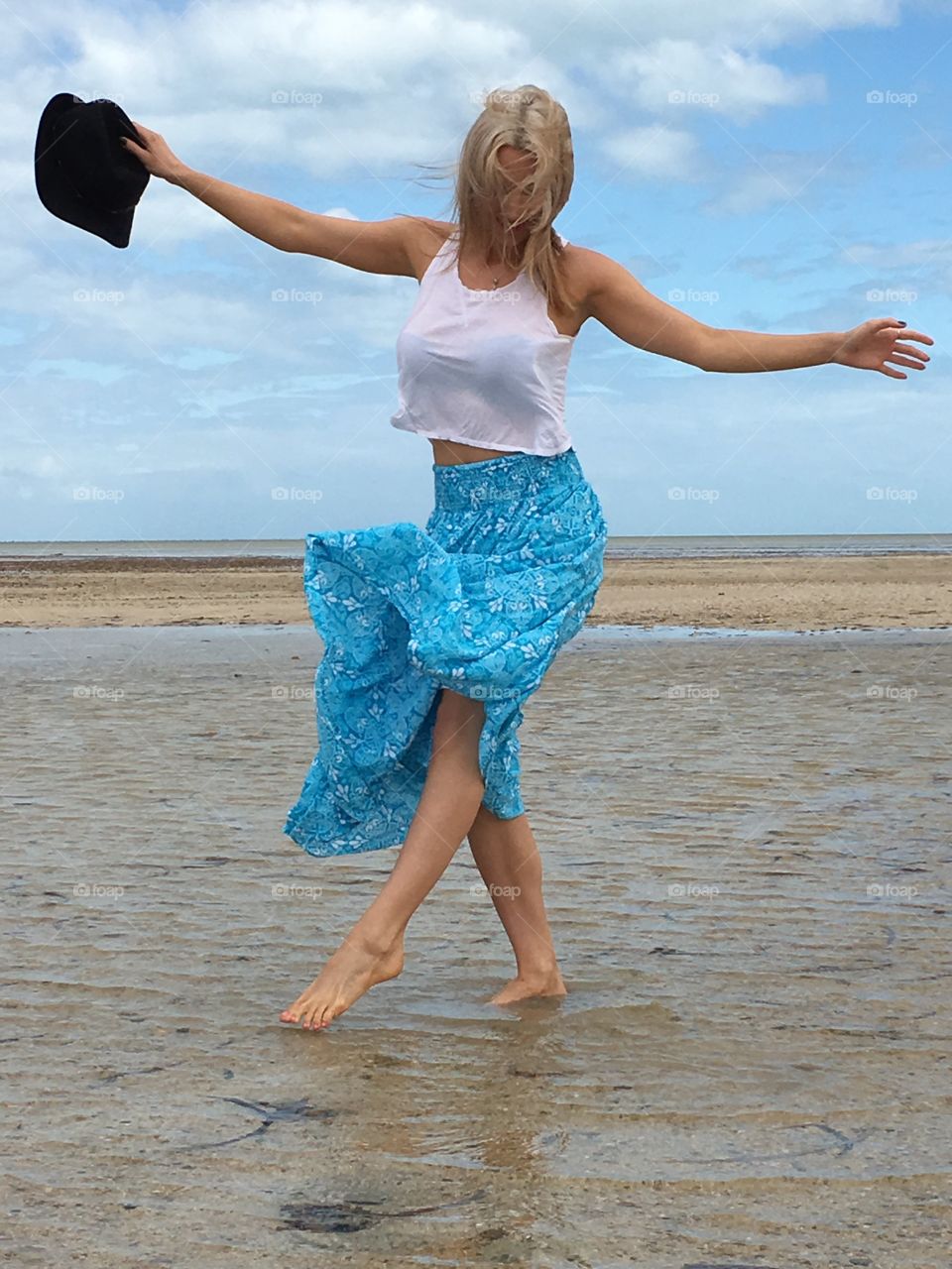 A barefoot blonde young woman in long flowing skirt in freeform expressive artistic dance on sand at south Australian beach