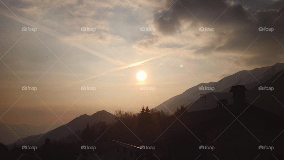 A hazy mountain mirage. The sun setting on a sunny but cool spring day in Italy, silhouetted mountains pan the landscape and clouds rally in the skies. Peaceful and still.