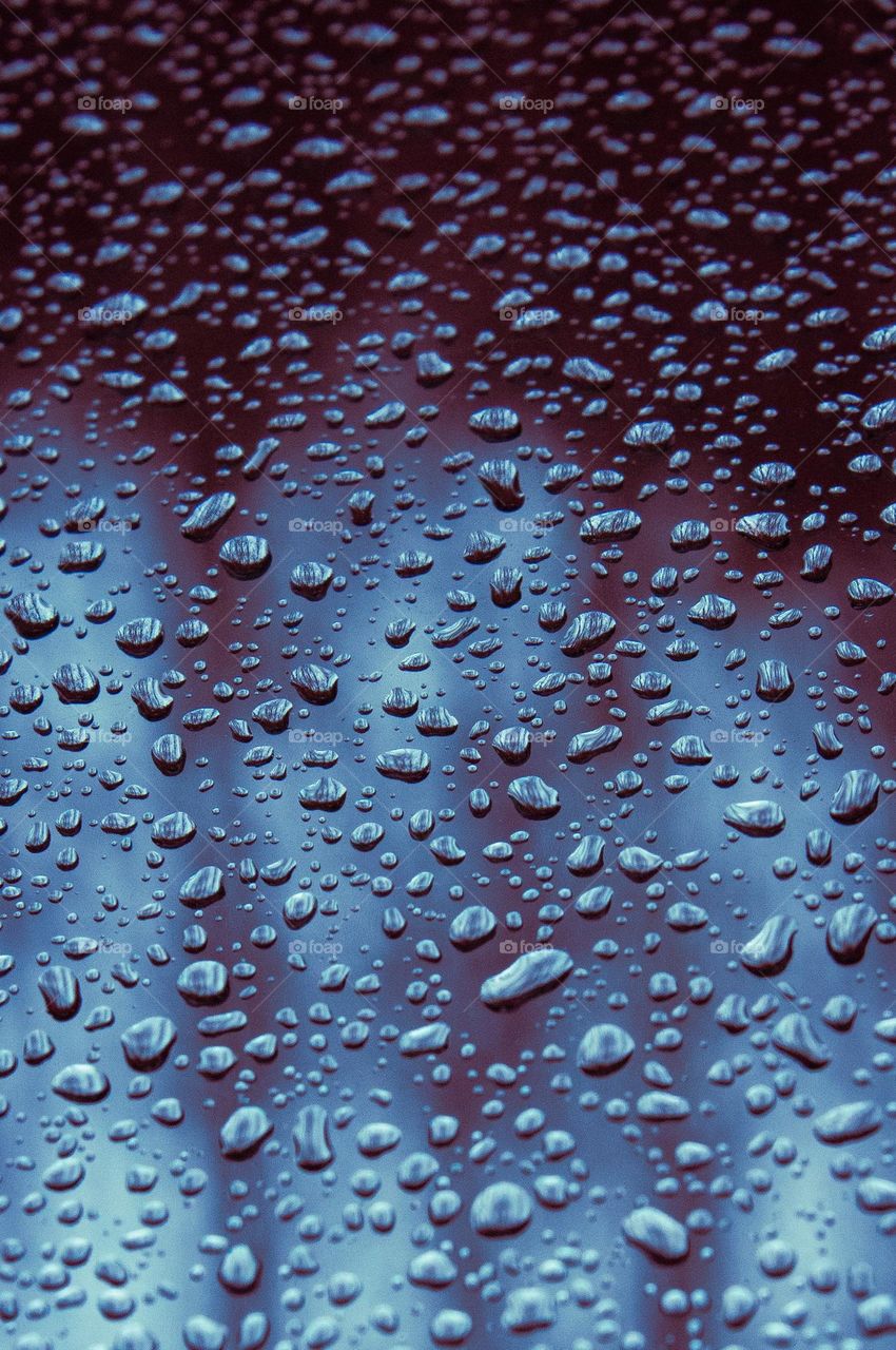 Reflections in the rain drops. Lots of raindrops on clear glass tinted different hues of blue.