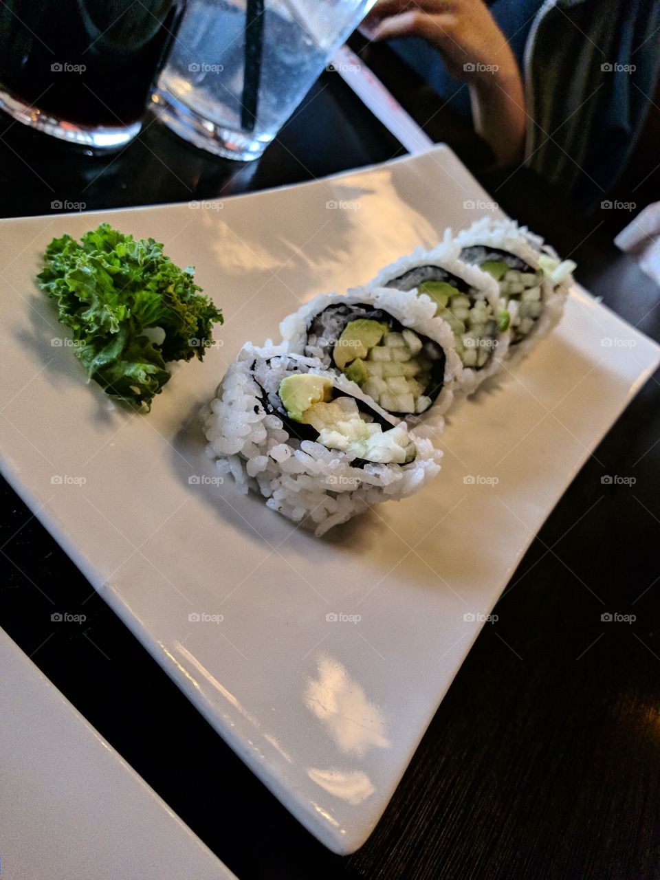 An underexposed avocado roll sits on a sushi plate