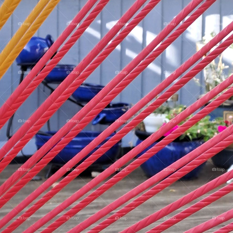 garden scene blue fence, pottery in background seen through a courful string chair